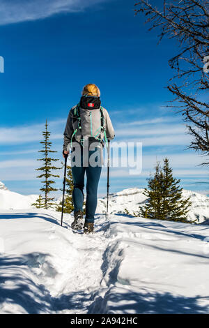 Female hiker on snow-covered pathway with snow-covered mountains, blue sky and clouds in the background; Lake Louise, Alberta, Canada Stock Photo