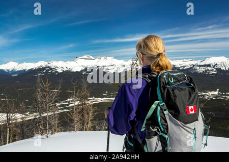 Female hiker on snow-covered pathway with snow-covered mountains, blue sky and clouds in the background; Lake Louise, Alberta, Canada Stock Photo