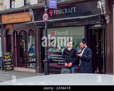 Men discussing business in the Hatton Garden jeweller's quarter in London, standing in front of a jewellery store. One man wearing kippah. Stock Photo