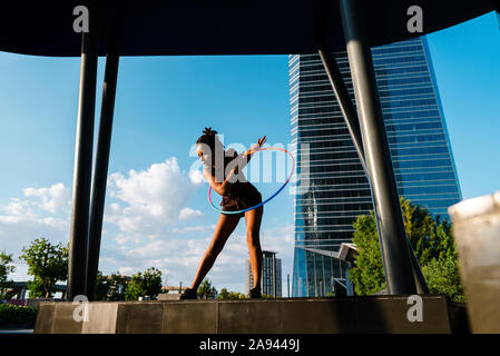 Low angle view of mixed race woman flying Hula Hoop in urban area Stock Photo