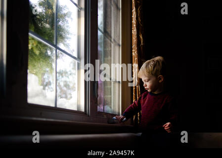 A little boy tries to open a window. Stock Photo