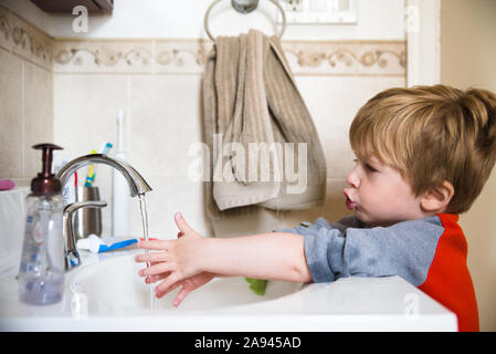 A little boy washes his hands in the bathroom sink. Stock Photo