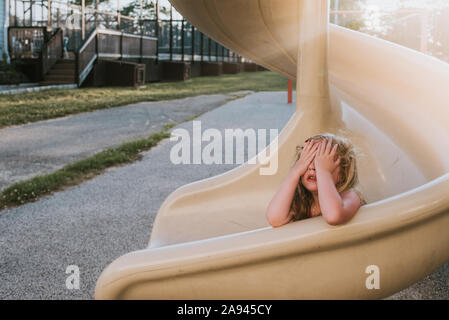 A little girl plays hide and seek on a slide. Stock Photo