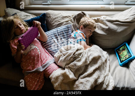 Two children lie on a couch and watch tablets. Stock Photo