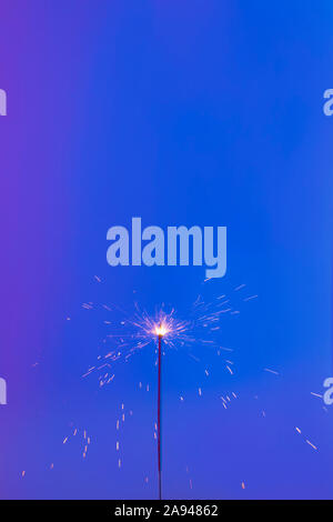 sparkler on a blue background. Short shutter speed. Small sparks scatter in different directions. Stock Photo