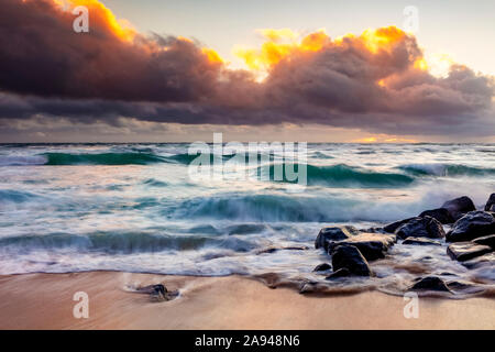 Sunrise over beach and ocean with tide washing up over sand and rocks; Kauai, Hawaii, United States of America Stock Photo