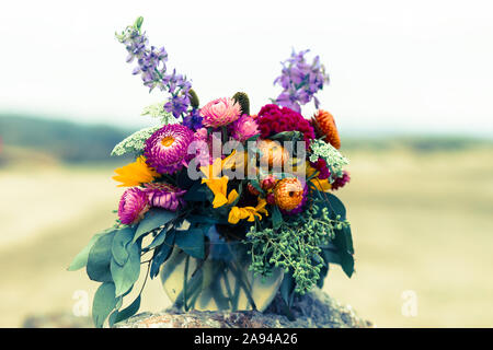 Bouquet of Chrysanthemums, Eucalyptus, Yellow and Lavender Colored Wildflowers on a Stone on a Foggy Afternoon, on a beach, at Half Moon Bay, CA Stock Photo