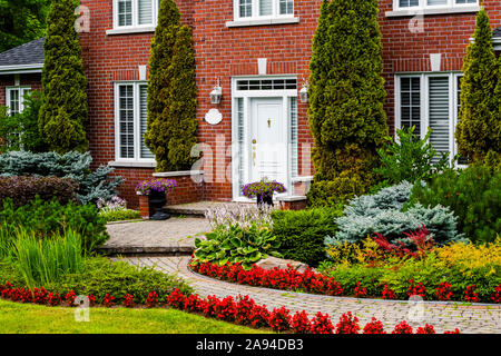 Stately brick house with a winding path and landscaping with plants and flowers in the front yard; Hudson, Quebec, Canada Stock Photo