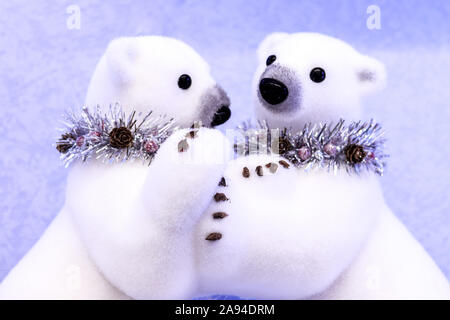 Two hugging white polar bears toys christmas decorations in necklaces from tinsel with pine cones on a snow background Stock Photo
