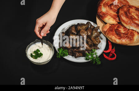 Grape vines leaves stuffed with meat, rice and vegetables with sour cream. Sarmale, dolma, sarma, golubtsy or golabki with cheese pies and sour cream. Stock Photo