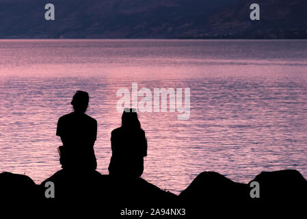 Close-up silhouettes of man and woman sitting together on beach watching sunset Stock Photo