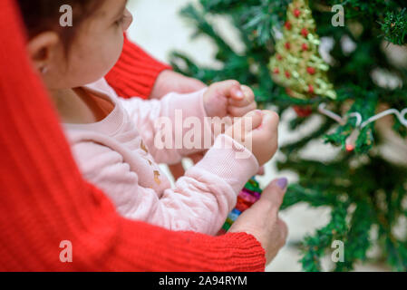 Two generation. Grandmother and grandchild decorate the Christmas tree with baubles indoors. The morning before Christmas. Happy family moments. Stock Photo