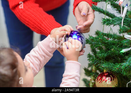 Two generation. Grandmother and grandchild decorate the Christmas tree with baubles indoors. The morning before Christmas. Happy family moments. Stock Photo