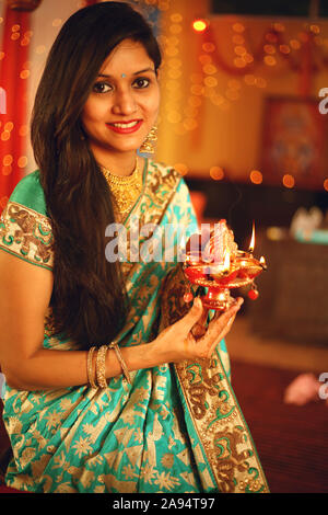 A beautiful young Indian couple in traditional sari dress holding a oil lamp light or diya with in decorative background on the occasion of Stock Photo