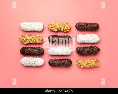 Set of different homemade eclairs on pink background. Top view of delicious healthy profitroles with different decor - chocolate, peanut and sherdded coconut Stock Photo