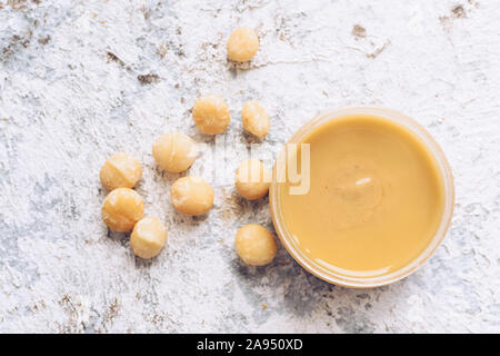 Macadamia nut butter in glass jar. Homemade raw organic macadamia nuts paste on grey background. Healthy natural food concept. Top view. Stock Photo