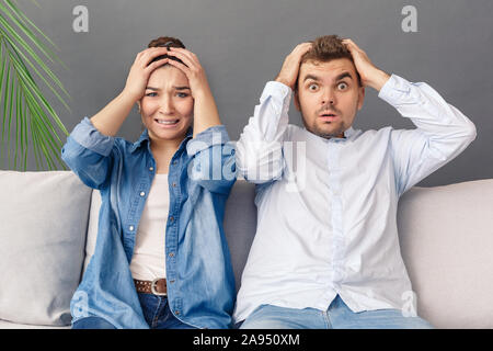 Relationnship Concept. Young couple sitting on sofa studio isolated on grey holding head shocked Stock Photo