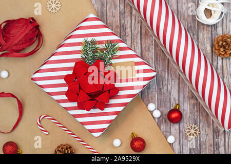 Flat lay concept for Christmas gift wrapping with beautiful red and white striped gift box with big red bow, wrapping paper, ribbons, and decoration l Stock Photo