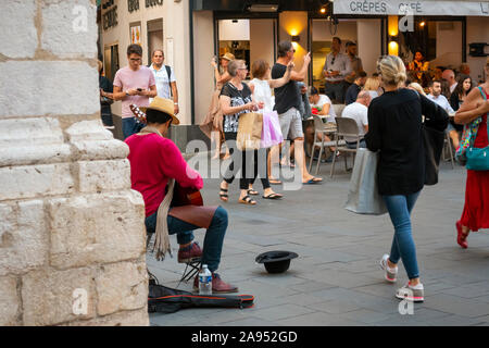 A young male street musician busking with a guitar plays for the crowd in the old town section of Nice, France. Stock Photo