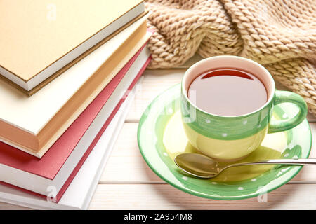 Still life on white wooden table top. Green cup of tea, spoon and stack of books in hard cover. Space for your text. Stock Photo