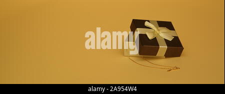 Decorative small gift box, half-open, with golden chain in and next to, close up, isolated on pastel yellow color background. Stock Photo