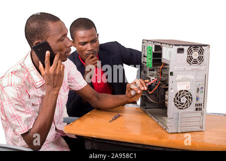 young computer technician talking on the phone and repairing a computer in front of an instructor Stock Photo