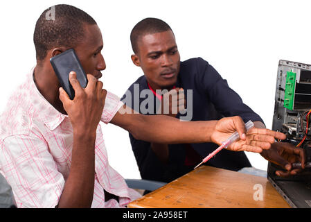 young computer technician talking on the phone and repairing a computer in front of an instructor Stock Photo