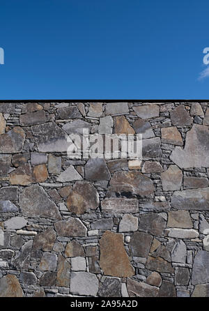 High stone wall in a landscape garden against a clear blue sky Stock Photo