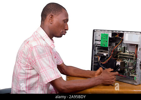 young technician sitting thinking with a desktop computer in front of him and holding a mobile phone. Stock Photo