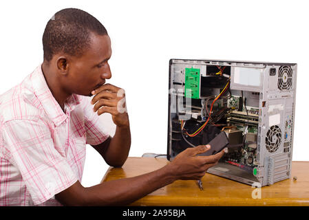 young technician sitting thinking with a desktop computer in front of him and holding a mobile phone. Stock Photo