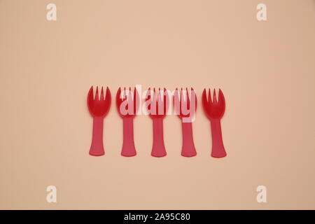Five red plastic forks lie next to each other isolated on pastel peach color background Stock Photo