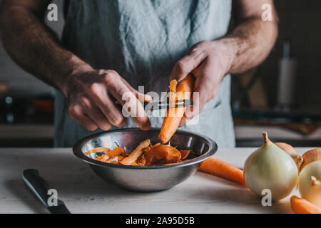 Closeup professional chef cleans and cuts ripe bright orange carrots with a special knife Stock Photo