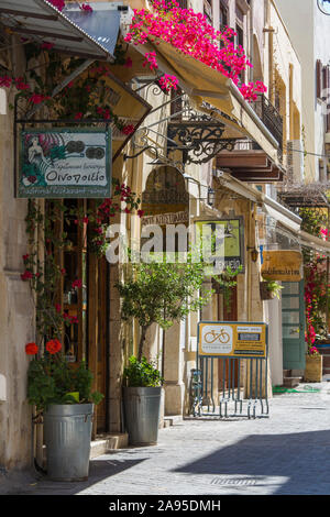 Chania, Crete, Greece. View along flower-filled Odos Hatzimihali Daliani, shop and restaurant signs prominent. Stock Photo