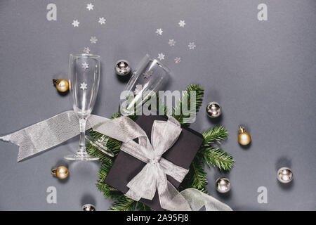 Christmas or winter composition. Black handmade gift boxes decorated with silver ribbon, tree branches, two glasses champagne confetti on gray backgro Stock Photo