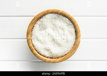 Grated coconut in bowl on white table. Top view. Stock Photo