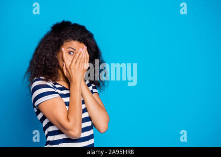 Photo of scared frightful girlfriend hiding her face to avoid negative emotions wearing striped t-shirt looking through hand near empty space isolated Stock Photo