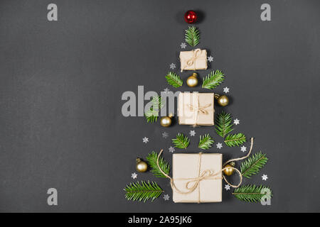 Christmas tree made from handmade gift boxes decorated with craft paper of fir tree branches and confetti on dark background. Flat lay, top view, copy Stock Photo
