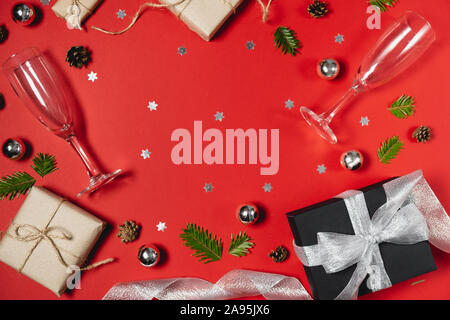 Christmas holiday composition. Handmade gift boxes decorated with craft paper of fir tree branches, two glasses champagne, pine and confetti on red ba Stock Photo