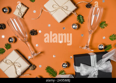 Christmas holiday composition. Handmade gift boxes decorated with craft paper of fir tree branches, two glasses champagne, pine and confetti on orange Stock Photo