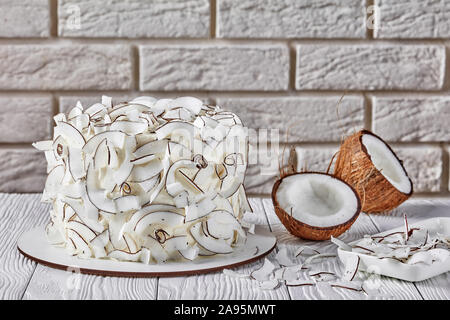 close-up of a coconut cake decorated with coconut ribbons with a brick wall at the background Stock Photo