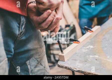 Carpentry workshop - master chisel makes a mounting hole for a spike in a wooden bar Stock Photo