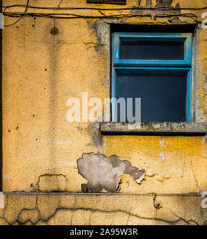 Old, faded yellow painted plaster and window on a building exterior. Stock Photo
