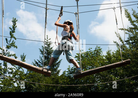 Ljubelj, Slovenia - July 28, 2007: A woman balances on suspended logs high above ground in an adrenaline park. Stock Photo