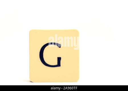 Dark letter G on a pale yellow square block isolated on white background Stock Photo