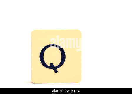 Dark letter Q on a pale yellow square block isolated on white background Stock Photo