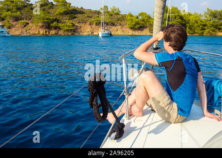 Rest on the sea, boat trip on a yacht. A young man in blue t-shirt sits on the deck and looks at the sea. Stock Photo