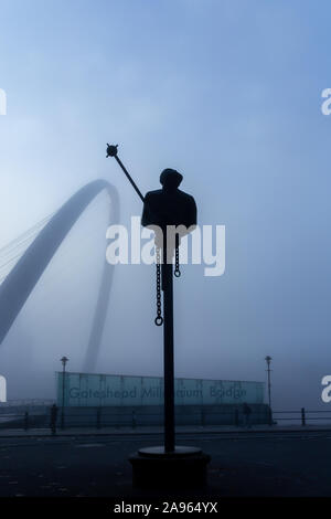 NEWCASTLE UPON TYNE, UK - NOVEMBER 09 2019: River God sculpture, by Andre Wallace, shrouded in fog with Gateshead Millennium Bridge in the background at the Quayside, Newcastle, UK Stock Photo