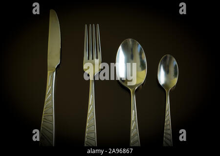 Still life of the kitchen objects. Silver knife, fork, spoon, teaspoon on the dark reflective backdrop. Stock Photo