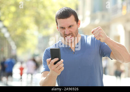 Front view portrait of an angry man checking crashed smart phone standing in the street Stock Photo