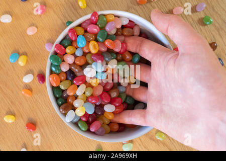 An adult man's hand scooping jelly beans in a bowl full of jellybeans. Concept, addiction to sweets, sweeties, candy, life's pleasures Stock Photo